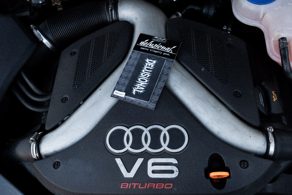 Duftbaum Produktbild von Delusional, mit Verpackung auf einer Motorhaube