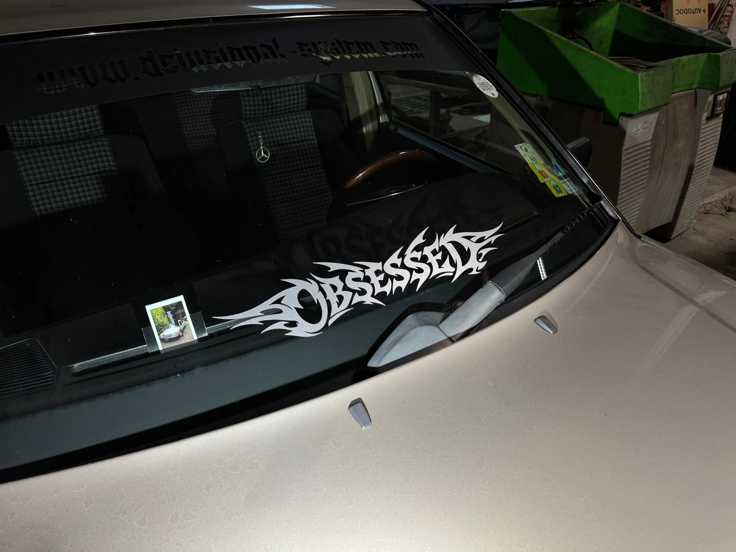 Sticker Obsessed in silbergrau glitzer auf der Frontscheibe eines Autos, weiter weg aufgenommen