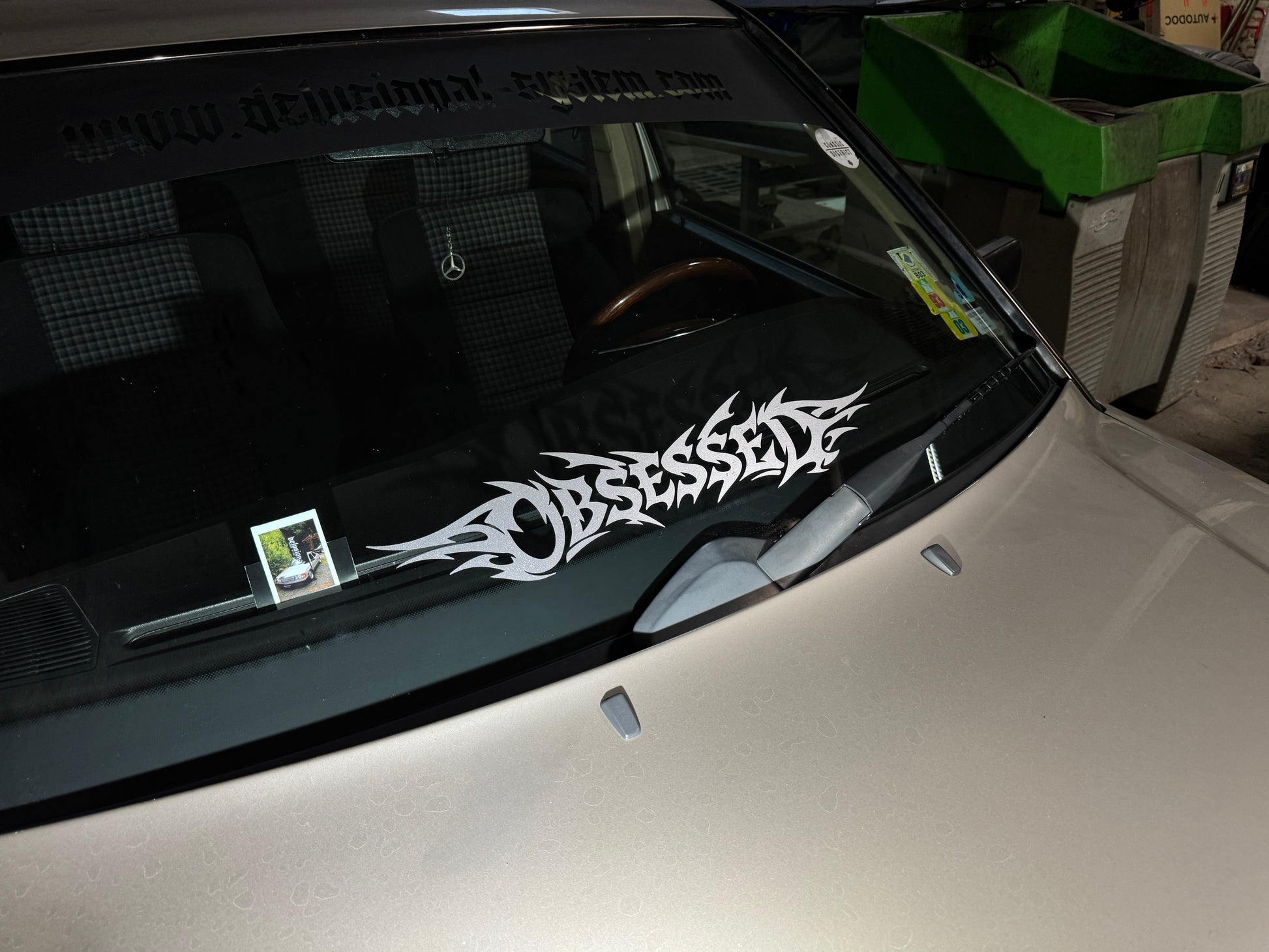 Sticker Obsessed in silbergrau glitzer auf der Frontscheibe eines Autos, weiter weg aufgenommen